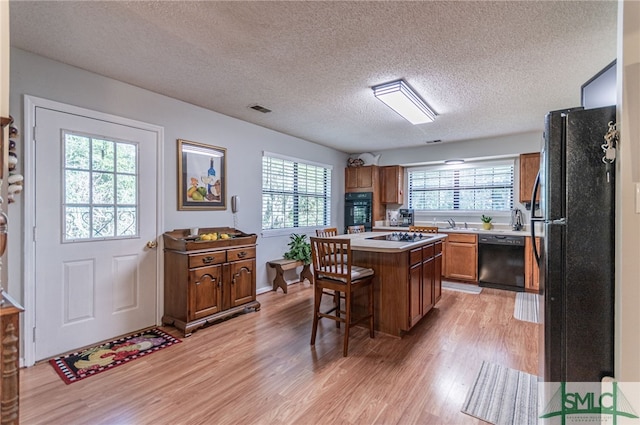 kitchen featuring a breakfast bar area, a center island, light hardwood / wood-style flooring, a textured ceiling, and black appliances