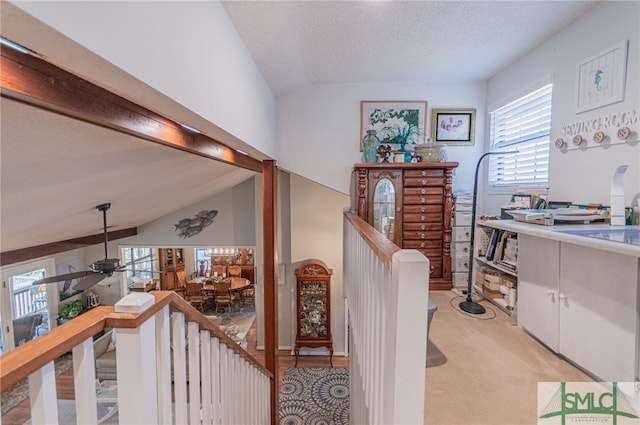 hallway featuring light colored carpet, vaulted ceiling, and a textured ceiling