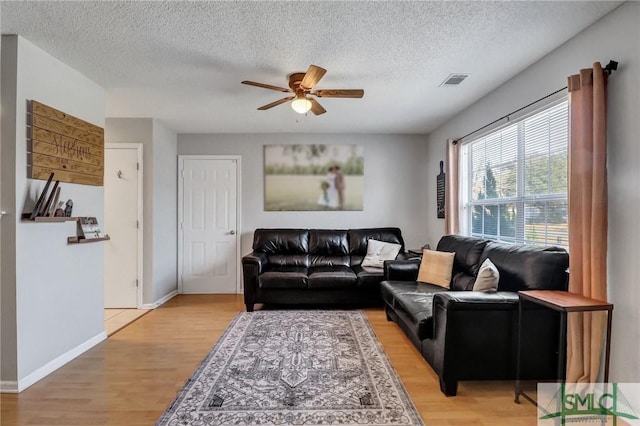 living room with ceiling fan, a textured ceiling, and light wood-type flooring