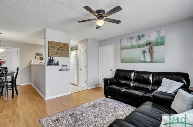 living room featuring ceiling fan, a textured ceiling, and light wood-type flooring