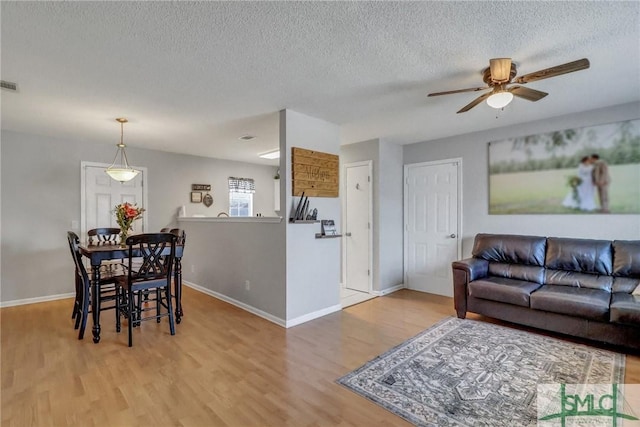 living room with ceiling fan, a textured ceiling, and light wood-type flooring