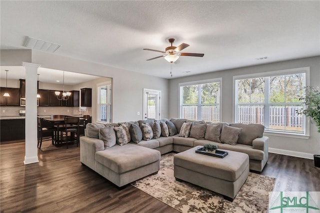 living room with ceiling fan with notable chandelier, dark hardwood / wood-style flooring, and decorative columns