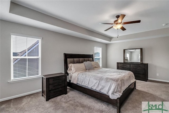 carpeted bedroom with ceiling fan and a raised ceiling