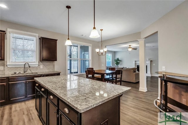 kitchen with dark brown cabinetry, sink, light stone counters, decorative light fixtures, and a kitchen island