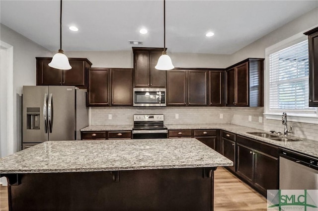 kitchen with a kitchen bar, sink, a center island, appliances with stainless steel finishes, and pendant lighting