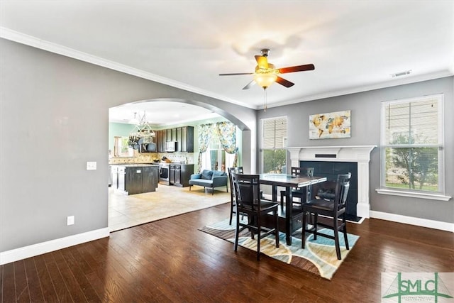 dining space with crown molding, dark wood-type flooring, a tile fireplace, and ceiling fan