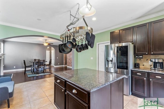 kitchen with light tile patterned floors, stainless steel fridge, dark brown cabinets, a kitchen island, and dark stone counters