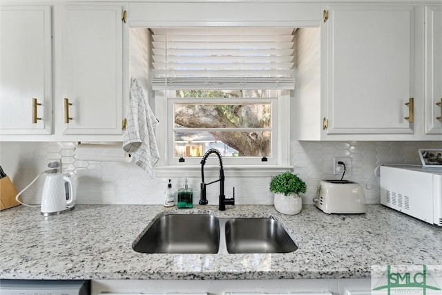 kitchen with light stone countertops, sink, white cabinets, and backsplash