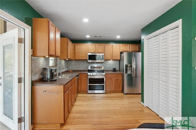 kitchen featuring appliances with stainless steel finishes, sink, decorative backsplash, and light hardwood / wood-style flooring