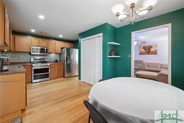 kitchen featuring sink, tasteful backsplash, an inviting chandelier, light wood-type flooring, and appliances with stainless steel finishes