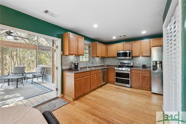kitchen with stainless steel appliances, sink, backsplash, and light wood-type flooring