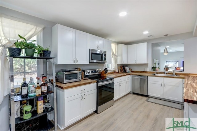 kitchen with decorative light fixtures, stainless steel appliances, wooden counters, and white cabinets