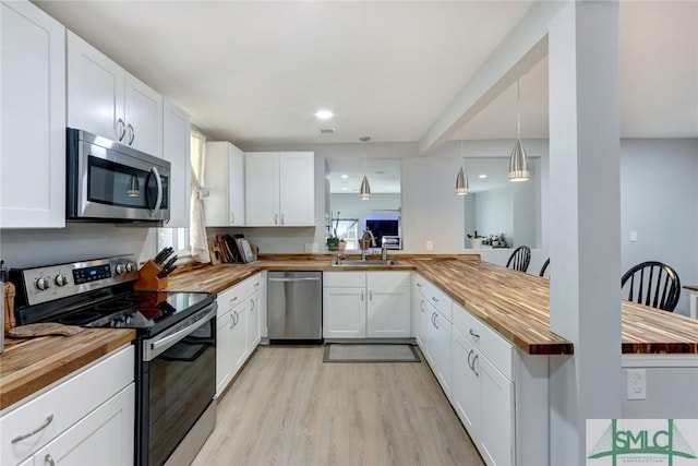 kitchen with butcher block counters, sink, white cabinetry, pendant lighting, and stainless steel appliances