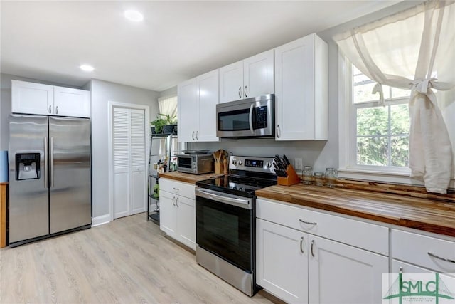 kitchen featuring butcher block countertops, light hardwood / wood-style flooring, white cabinets, and appliances with stainless steel finishes