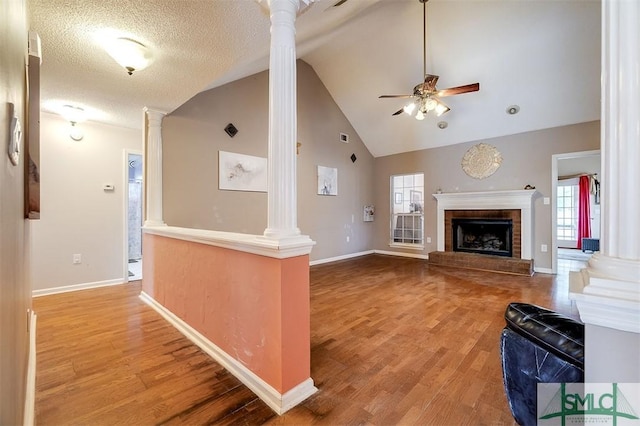 unfurnished living room with a brick fireplace, a textured ceiling, hardwood / wood-style floors, ceiling fan, and decorative columns