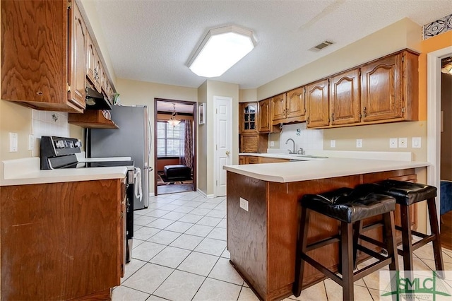 kitchen featuring a breakfast bar, light tile patterned floors, kitchen peninsula, electric stove, and backsplash