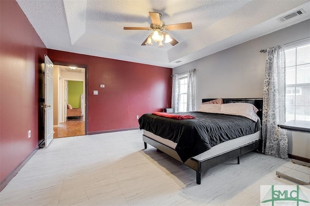 bedroom featuring ceiling fan, a tray ceiling, multiple windows, and a textured ceiling