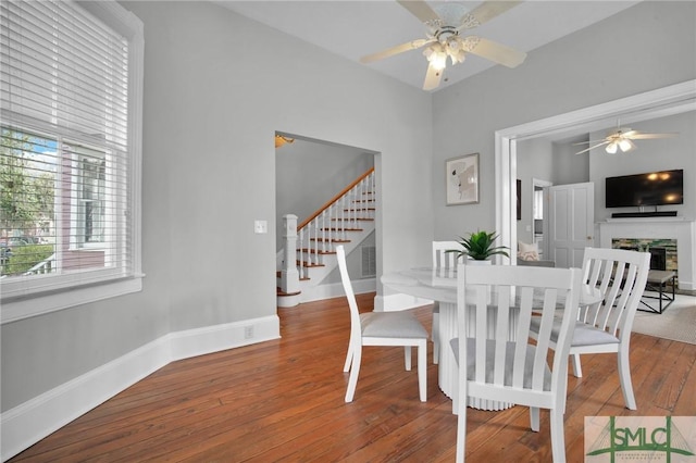 dining area featuring wood-type flooring, ceiling fan, and a fireplace