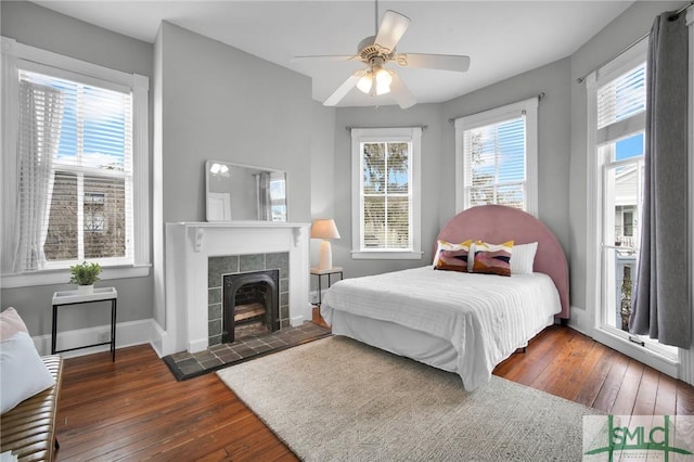 bedroom with a tiled fireplace, dark hardwood / wood-style floors, and ceiling fan