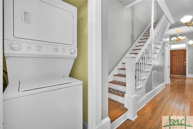 laundry room featuring stacked washer / drying machine, wood-type flooring, and a notable chandelier