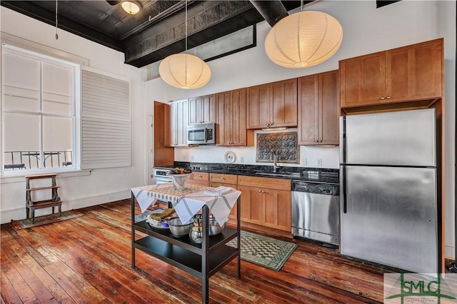 kitchen featuring dark wood-type flooring, sink, hanging light fixtures, appliances with stainless steel finishes, and a towering ceiling