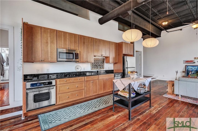 kitchen featuring sink, hanging light fixtures, dark hardwood / wood-style flooring, a towering ceiling, and stainless steel appliances