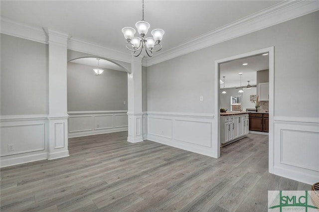 unfurnished dining area with crown molding, an inviting chandelier, light hardwood / wood-style floors, and decorative columns