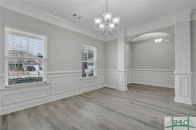 unfurnished dining area featuring crown molding, light hardwood / wood-style flooring, decorative columns, and a chandelier