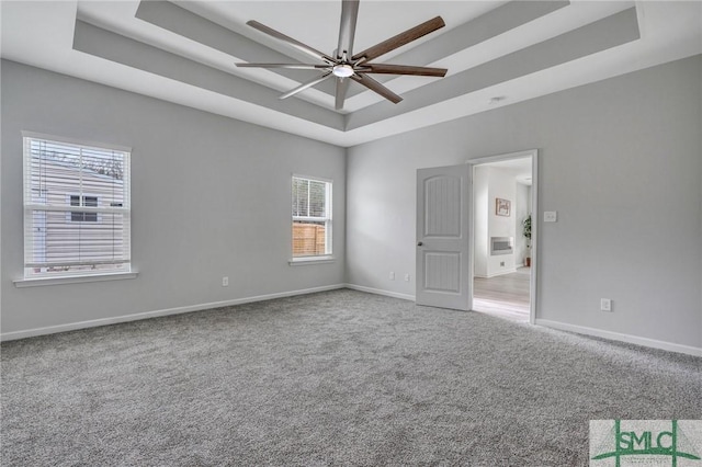 carpeted spare room with a raised ceiling and ceiling fan