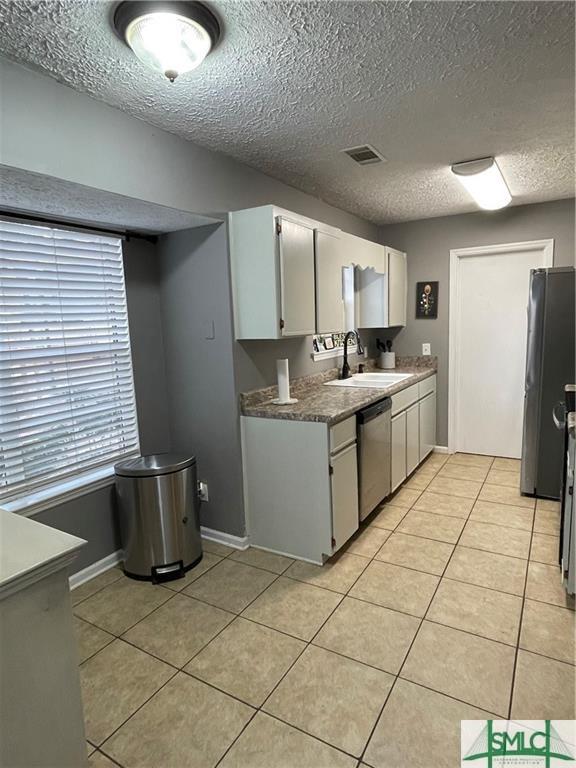 kitchen with light tile patterned flooring, dishwasher, sink, white cabinets, and fridge