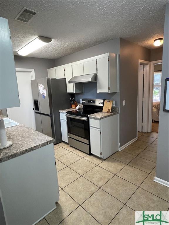 kitchen featuring appliances with stainless steel finishes, light tile patterned floors, a textured ceiling, and white cabinets