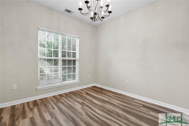 empty room featuring an inviting chandelier and hardwood / wood-style flooring