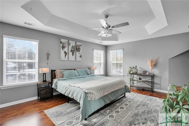 bedroom with dark wood-type flooring, ceiling fan, a tray ceiling, and multiple windows