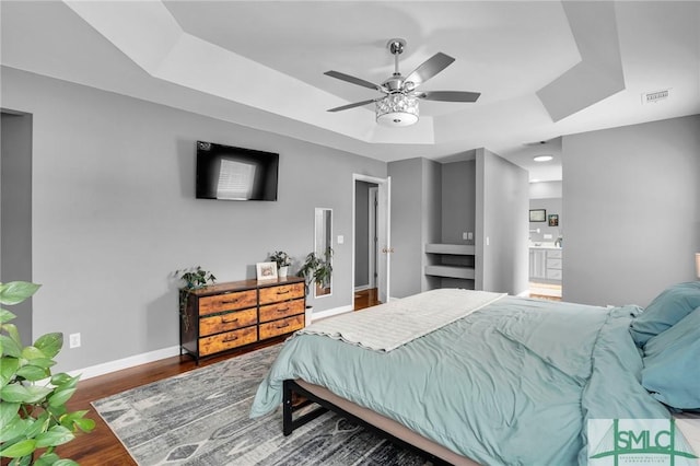 bedroom featuring connected bathroom, a tray ceiling, dark hardwood / wood-style floors, and ceiling fan