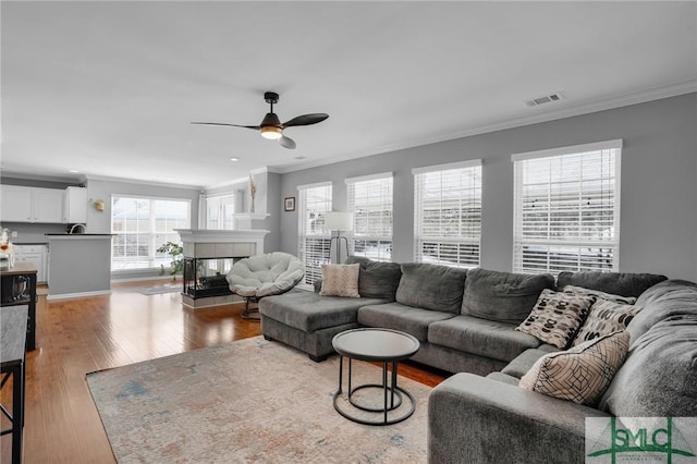 living room with a tiled fireplace, crown molding, and light wood-type flooring