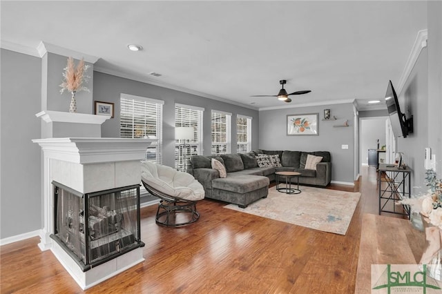 living room with a tiled fireplace, crown molding, wood-type flooring, and ceiling fan