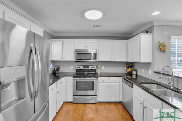 kitchen featuring sink, white cabinets, dark stone counters, stainless steel appliances, and crown molding