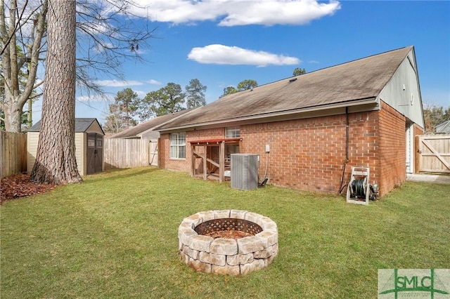 rear view of house with a storage shed, an outdoor fire pit, a yard, and central air condition unit