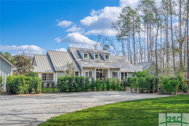 view of front of property with gravel driveway, a front yard, a standing seam roof, metal roof, and fence