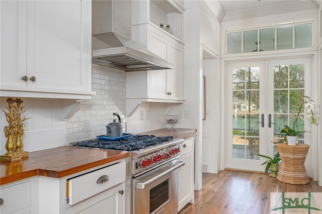 kitchen featuring tasteful backsplash, wall chimney range hood, stainless steel range, and a healthy amount of sunlight