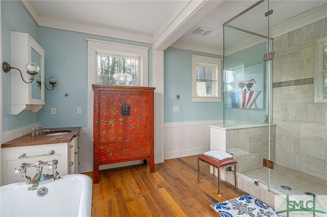 bathroom with a wainscoted wall, wood finished floors, visible vents, ornamental molding, and a shower stall