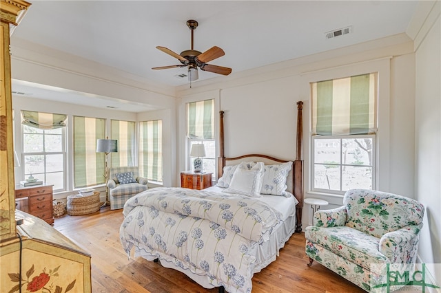 bedroom featuring light wood-type flooring, multiple windows, visible vents, and ornamental molding