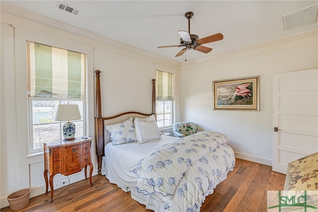 bedroom with a ceiling fan, wood-type flooring, visible vents, and ornamental molding