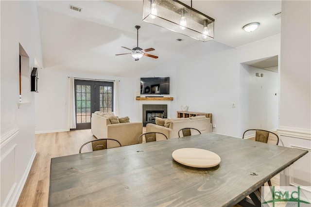 dining area featuring french doors, lofted ceiling, light hardwood / wood-style flooring, a tile fireplace, and ceiling fan