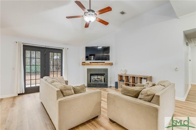 living room featuring ceiling fan, lofted ceiling, a tile fireplace, and light hardwood / wood-style flooring