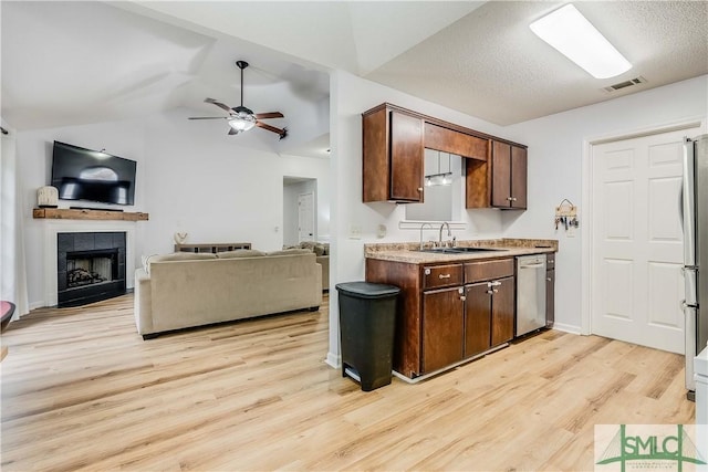 kitchen with appliances with stainless steel finishes, lofted ceiling, sink, a tiled fireplace, and light hardwood / wood-style flooring