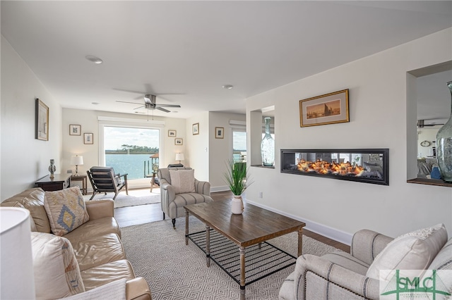 living room with a multi sided fireplace, light wood-type flooring, ceiling fan, and a water view