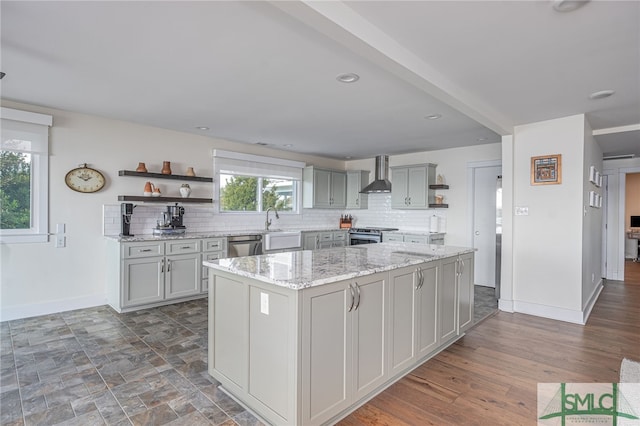 kitchen featuring gray cabinets, stainless steel appliances, light stone countertops, a kitchen island, and wall chimney exhaust hood