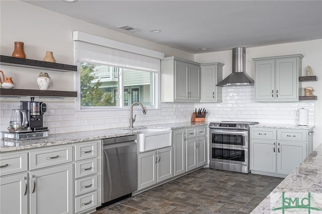 kitchen with wall chimney range hood, sink, appliances with stainless steel finishes, light stone counters, and tasteful backsplash