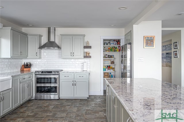 kitchen with gray cabinets, light stone countertops, appliances with stainless steel finishes, and wall chimney exhaust hood